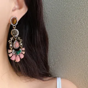 Vintage ornate dangle earrings with pink resin stones and rhinestones worn by a model