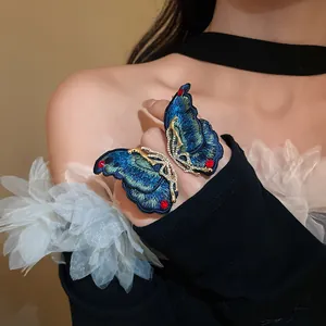 Detailed macro view of an intricate blue embroidered butterfly earring with gold plating.