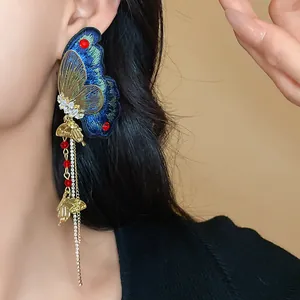 Detailed view of long butterfly tassel earring with blue embroidery and red beads
