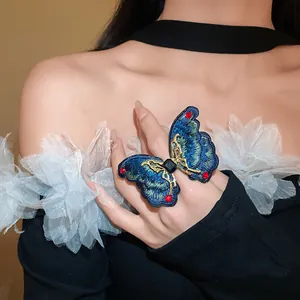 Detailed view of a large blue embroidered butterfly ring with red crystal accents