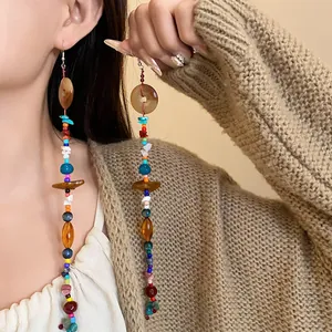Dettaglio di lunghi orecchini etnici con pietre naturali colorate e perline in stile boho