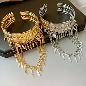 Dettaglio di bracciali a polsino con nappe di piume oro e argento su supporto.