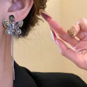 Close-up detail of silver butterfly tassel earrings with zircon and shell inlay