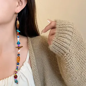 Primo piano di un lungo orecchino di pietre naturali colorate in stile etnico su modella