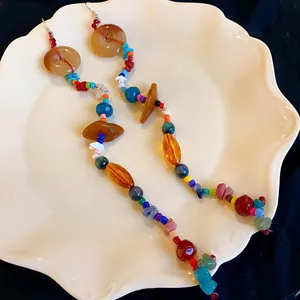 Dettaglio orecchini boho lunghi con perline colorate e pietre naturali su piatto bianco