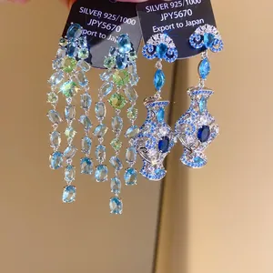 Close-up of blue and green zircon tassel and vase-shaped earrings on display cards.
