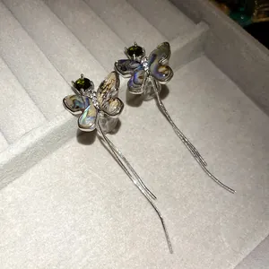 Macro close-up of butterfly earrings with green zircon and iridescent shell wings