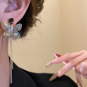Detailed close-up of 18K gold plated butterfly earring with shell inlay and long tassels
