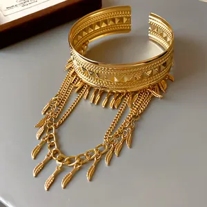 Dettaglio ravvicinato di un bracciale a fascia dorato con nappe a piuma e foglie moda