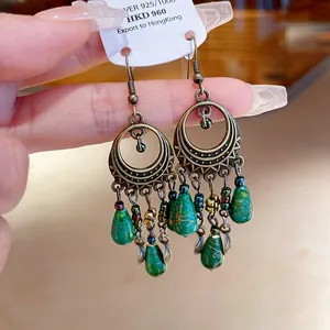 Primo piano di eleganti orecchini etnici a goccia con pietre verdi e cerchi in bronzo.