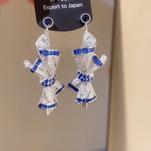 Macro detail showing silver ribbon earrings with sparkling blue and white zircon stones