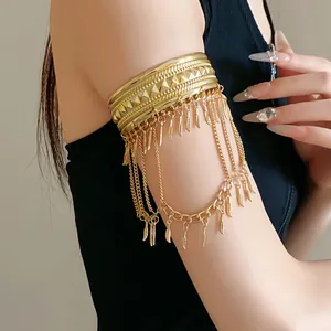 Dettaglio del bracciale bohémien dorato con nappe di piume e catene sul braccio superiore.