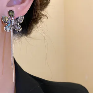 Close-up of shell butterfly earrings with green zirconia and long chain tassels on ear