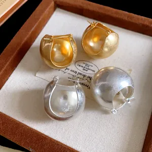 Macro detail of chunky gold and silver geometric bowl shaped hoop earrings in jewelry box