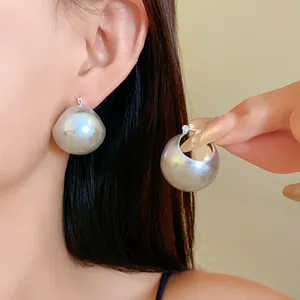 Close-up detail of minimalist silver chunky hoop earrings worn by model and held by hand.
