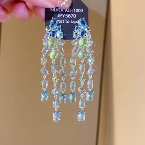 Detailed view of long silver tassel earrings with blue and green zirconia stones