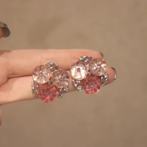 Gros plan de boucles d'oreilles fleurs roses avec cristaux portées à la main.