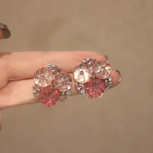 Vue rapprochée détaillée de boucles d'oreilles fleurs roses et pêche tenues à la main