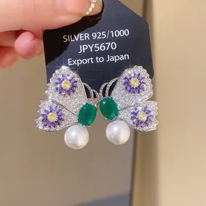 Close-up detail of butterfly earrings featuring purple flowers and elegant pearl drops