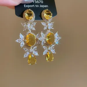 Close-up of silver needle zircon earrings with yellow stones and butterfly motifs.
