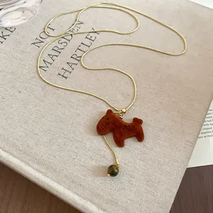 Détail d'un collier chaîne serpent doré avec pendentif cheval en velours brun et perle.