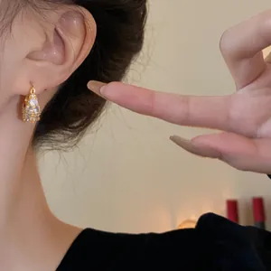 Close-up detail showing gold-plated geometric hoop earring with sparkling zircons on model's ear