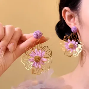 Detailopname van paarse raffia en goudkleurige bloemenoorbellen, gedragen en vastgehouden.