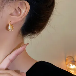 Close-up of gold-plated geometric hoop earring with sparkling zircons on model's ear.