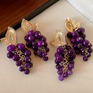 Dettaglio di orecchini vintage a forma di uva viola con foglie d'oro e strass brillanti