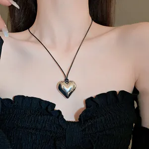 Primo piano di una collana con ciondolo a cuore in argento minimalista su un cordino nero