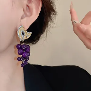 Primo piano di orecchini vintage a grappolo d'uva con perle viola e foglia di cristallo.