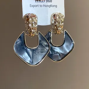 Dettaglio macro di orecchini stile retrò con metallo martellato e resina marmorizzata.
