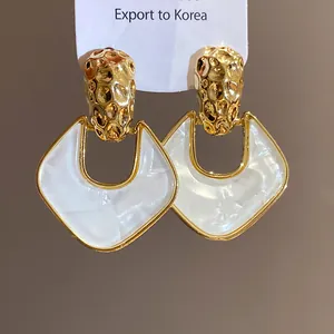 Dettaglio di orecchini vintage in oro martellato e forma geometrica bianca elegante