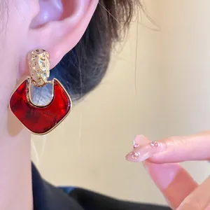 Dettaglio di orecchini geometrici rossi vintage con finitura in oro martellato su modella.
