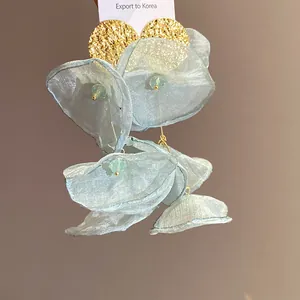 Close-up detail of blue chiffon flower tassel earrings with gold textured studs.