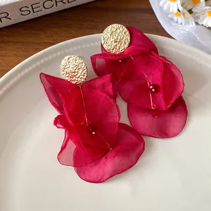 Macro shot of red chiffon flower tassel earrings with gold textured studs on beige plate.