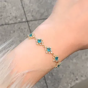 Detail of elegant gold bracelet with blue zircon diamond-shaped floral links on wrist.