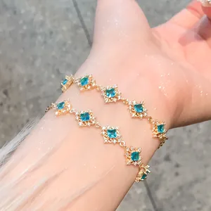 Detail view of a luxury gold bracelet featuring blue square zircon flower charms on wrist.