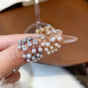 Close-up detail of multilayer zircon and pearl open rings in gold and silver finishes.
