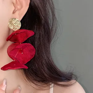 Macro detail of large red chiffon flower tassel earrings with textured gold stud on model