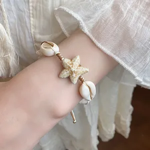 Close-up of bohemian style starfish and cowrie shell braided bracelet on wrist