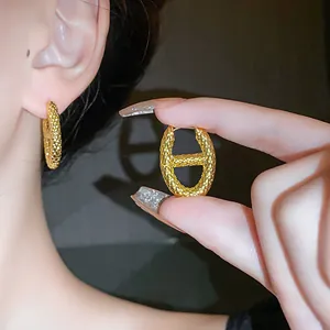 Close-up view of textured gold elliptical hoop earrings with unique snake skin pattern.