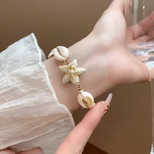Close-up detail of a handmade braided bracelet featuring natural shells and ceramic starfish