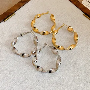 Elegant oversized twisted spiral hoop earrings in gold and silver finish with silver needles