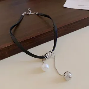 Gros plan détaillé des pendentifs en perle blanche et boule argentée sur un tour de cou en cuir