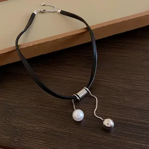Gros plan sur un choker en cuir noir minimaliste avec pendentifs perle et bille argentée