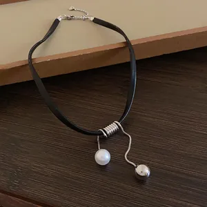 Gros plan d'un choker minimaliste en cuir noir avec breloques perle et boule argentée