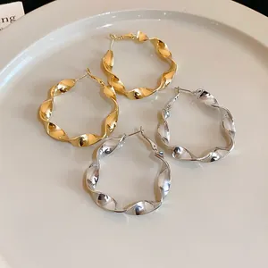 Close-up detail of elegant twisted spiral hoop earrings in gold and silver finishes.