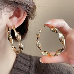 Detailed close-up view of elegant twisted gold spiral hoop earrings worn on an ear