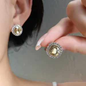 Dettaglio di orecchini tondi dorati con cristallo champagne e alone di strass